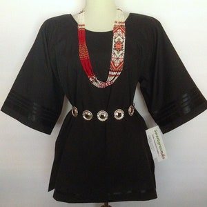 May include: A black tunic with long sleeves and a round neckline. The tunic has a silver belt with round decorative accents. The model is wearing a beaded necklace with red, white, and orange beads.