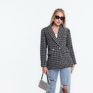 Può includere: Un blazer a quadri bianco e nero con chiusura a doppio petto e due tasche anteriori. Il blazer è indossato sopra una t-shirt bianca e abbinato a jeans blu chiaro strappati e sneakers bianche.