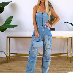 May include: A light blue denim jumpsuit with a strapless top and cargo pockets. The jumpsuit is worn by a person with long blonde hair and is paired with a light blue handbag.
