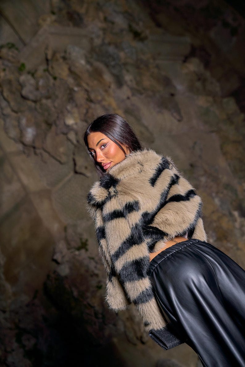 May include: A faux fur jacket with a tan base and bold black stripes. The jacket is paired with black leather pants. The overall look is stylish and modern, suitable for a fashion-forward wardrobe.
