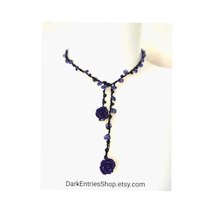 May include: A dark purple necklace with a Y-shaped design. The necklace features dark purple rose pendants and small purple beads strung on a black cord. The text "DarkEntriesShop.etsy.com" is at the bottom.