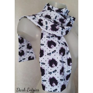 May include: White scarf with a repeating pattern of black and white eyes and a person's face with dark hair. The background is white with black polka dots.