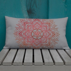 May include: A white throw pillow with a red and orange mandala design. The mandala features a star with a circle in the center.