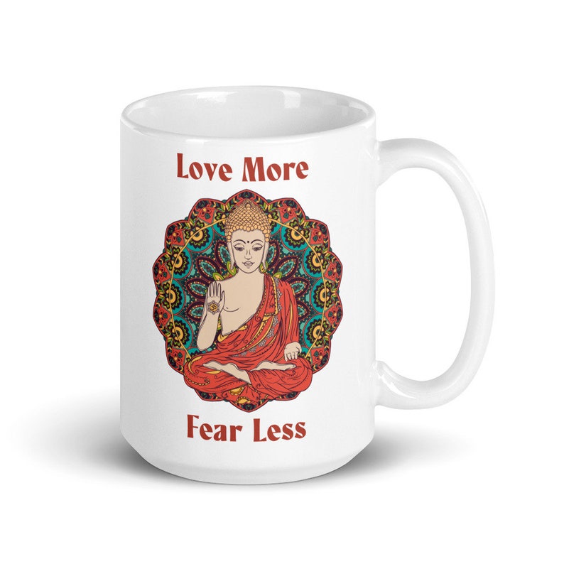 love more fear less coffee mug with handle by goddess swag. colorful buddha image with mandala behind it. Love More is written in a deep red above the buddha image and fear less is written in a deep red below the buddha image. Double sided.