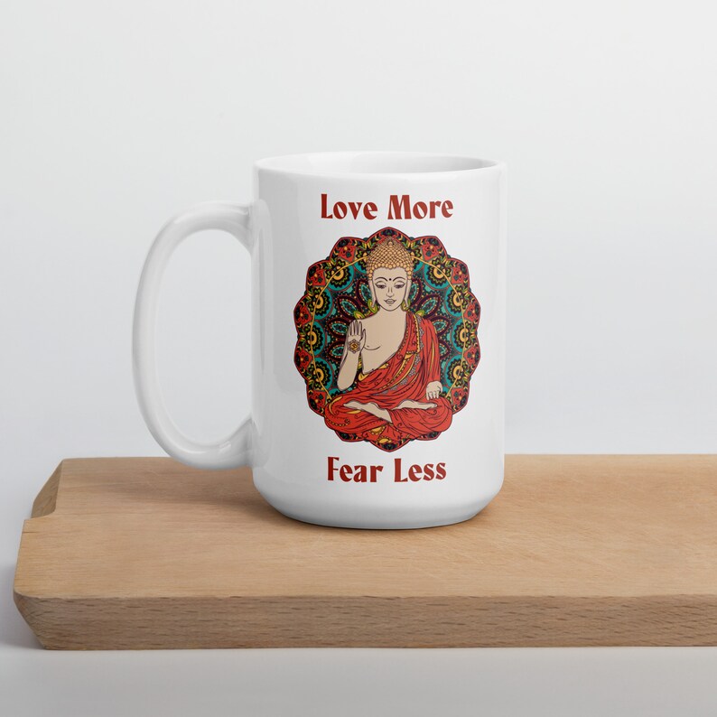 love more fear less coffee mug with handle by goddess swag. colorful buddha image with mandala behind it. Love More is written in a deep red above the buddha image and fear less is written in a deep red below the buddha image. Double sided.
