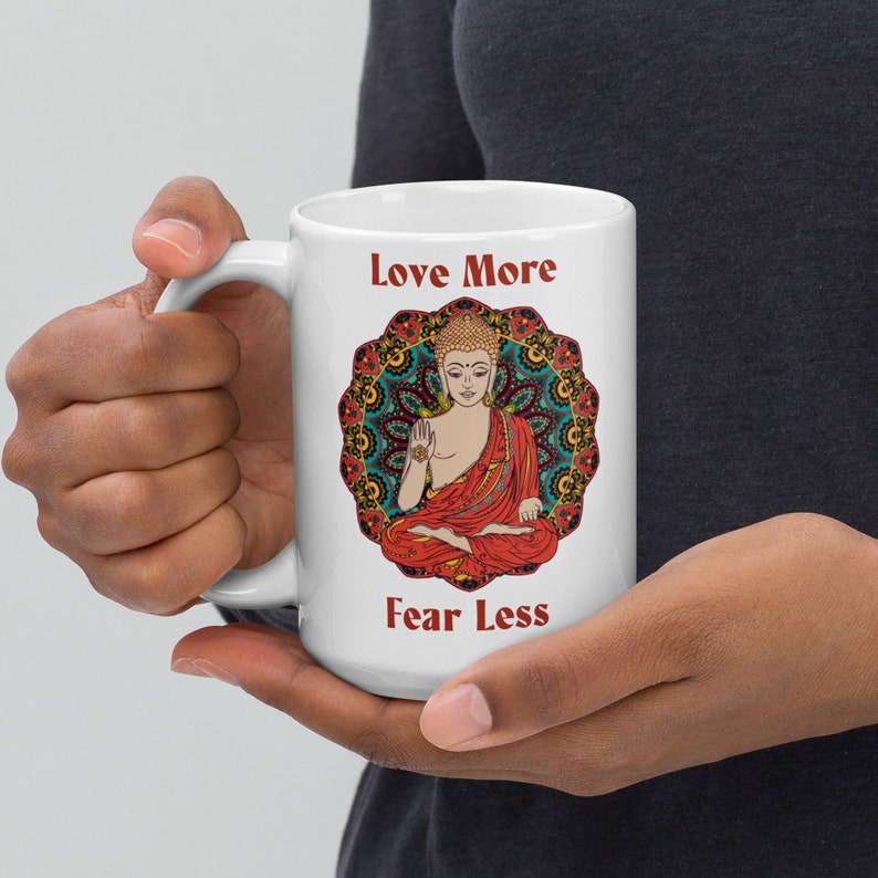 love more fear less coffee mug with handle by goddess swag. colorful buddha image with mandala behind it. Love More is written in a deep red above the buddha image and fear less is written in a deep red below the buddha image. Double sided.