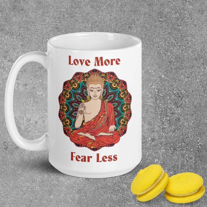 love more fear less coffee mug with handle by goddess swag. colorful buddha image with mandala behind it. Love More is written in a deep red above the buddha image and fear less is written in a deep red below the buddha image. Double sided.
