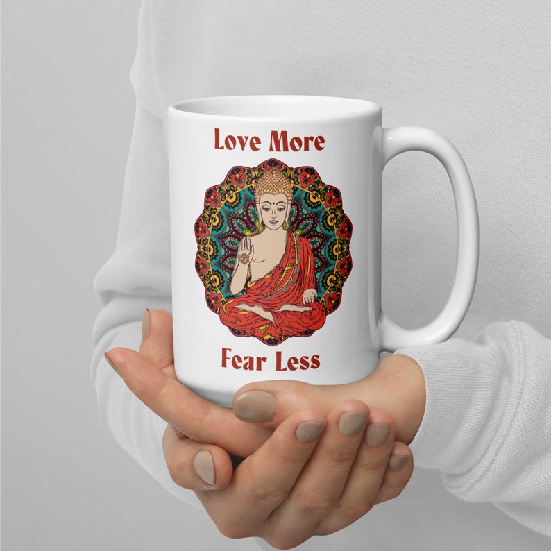 love more fear less coffee mug with handle by goddess swag. colorful buddha image with mandala behind it. Love More is written in a deep red above the buddha image and fear less is written in a deep red below the buddha image. Double sided.
