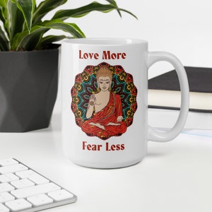 love more fear less coffee mug with handle by goddess swag. colorful buddha image with mandala behind it. Love More is written in a deep red above the buddha image and fear less is written in a deep red below the buddha image. Double sided.