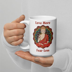 love more fear less coffee mug with handle by goddess swag. colorful buddha image with mandala behind it. Love More is written in a deep red above the buddha image and fear less is written in a deep red below the buddha image. Double sided.