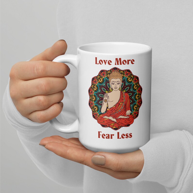 love more fear less coffee mug with handle by goddess swag. colorful buddha image with mandala behind it. Love More is written in a deep red above the buddha image and fear less is written in a deep red below the buddha image. Double sided.