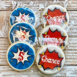 May include: Six round sugar cookies decorated with red, white, and blue comic book-style designs. Two cookies feature the word "Chance" in a red speech bubble. Four cookies feature a red number "5" in a blue speech bubble.