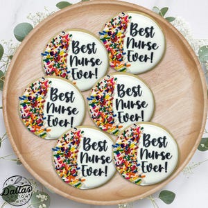 May include: Six round sugar cookies decorated with white frosting and colorful sprinkles. Each cookie has the text "Best Nurse Ever!" written in black frosting.