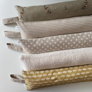 May include: Five different doorstops, each with a unique fabric pattern. The doorstops are made of a soft, plush material and are perfect for protecting your walls and doors from damage. The doorstops are arranged in a stack, with the top doorstop being a green fabric with a white polka dot pattern and a rabbit design. The second doorstop is a beige fabric with white stripes. The third doorstop is a beige fabric with white stars. The fourth doorstop is a white fabric with a fuzzy texture. The fifth doorstop is a yellow fabric with a white pattern.