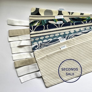 May include: Several fabric samples with diverse patterns and colours, such as stripes, floral, and geometric designs. Each piece has a white tag and is accompanied by white and beige fabric straps. The image also includes a "SECONDS SALE" sticker.