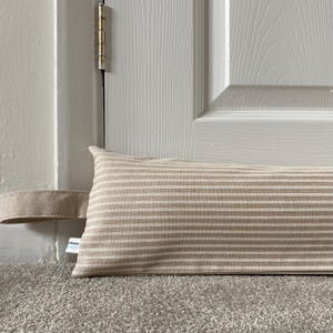 May include: A beige and white striped doorstop with a fabric loop. The doorstop is placed at the bottom of a white door.