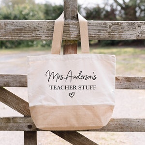 May include: A beige canvas tote bag with brown handles. The bag has the text "Mrs. Anderson's Teacher Stuff" printed in black with a small heart symbol.
