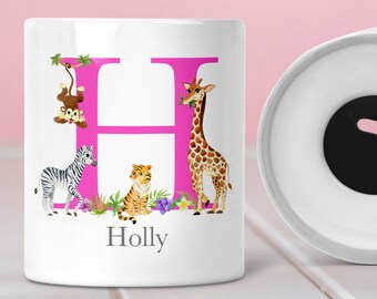 May include: White ceramic money box with a pink letter H decorated with jungle animals, including a giraffe, zebra, monkey, and tiger. The name "Holly" is written below the letter.