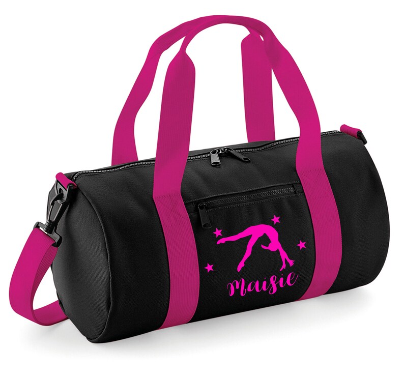 May include: Black gym bag with pink straps and a pink silhouette of a gymnast doing a back handspring. The bag has a zippered pocket on the front and the name "Maisie" is printed on the front.