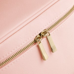 Pode incluir: Close-up de um z&iacute;per rosa com puxadores dourados. O z&iacute;per est&aacute; em uma bolsa de tecido rosa.
