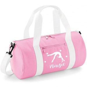 May include: Pink gym bag with white straps and a white silhouette of a gymnast doing a back handspring. The bag has white stars and the name "Maisie" printed on it.