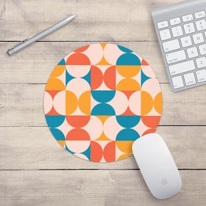 May include: A round mouse pad with a geometric pattern of orange, blue, and white semi-circles on a pink background.