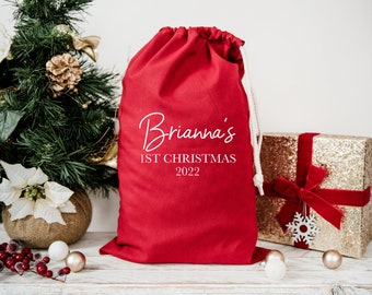 May include: Red Christmas gift bag with white drawstring and the text "Brianna's 1st Christmas 2022" printed on the front.
