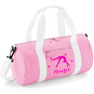 May include: Pink gym bag with white straps and a zipper closure. The bag has a pink gymnast silhouette with stars and the name "Maisie" printed on it.