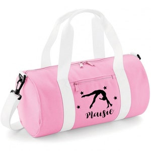 May include: Pink gym bag with white straps and a black silhouette of a gymnast doing a back handspring. The bag has a zippered pocket and the name "Maisie" is printed on the front.