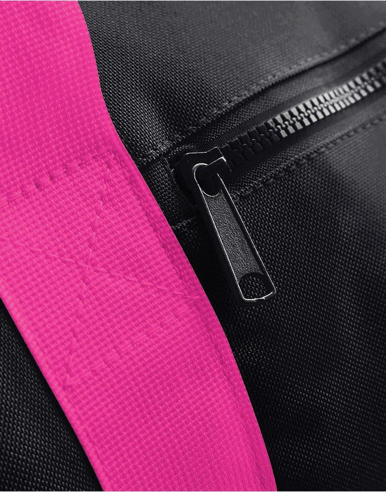 May include: Close-up of a black zipper on a black bag with a bright pink strap.