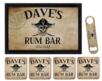 Puede incluir: Un conjunto de accesorios de bar con temática pirata. El conjunto incluye una estera de bar, cuatro posavasos y un abridor de botellas. La estera de bar y los posavasos presentan un diseño de calavera y huesos cruzados con el texto "Dave's Rum Bar Est 2022". El abridor de botellas está hecho de madera y tiene un diseño de brújula.