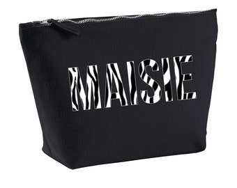 Könnte beinhalten: Schwarze Kosmetiktasche aus Canvas mit Reißverschluss, weißem Zebra-Muster und dem Namen "MAISIE" in Weiß gedruckt.