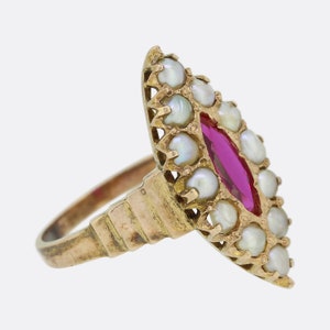 May include: A gold ring with a red gemstone surrounded by white pearls. The ring has a delicate, ornate design.