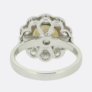 May include: A silver ring with a large pearl surrounded by a halo of smaller diamonds. The ring is set in a flower-shaped design.