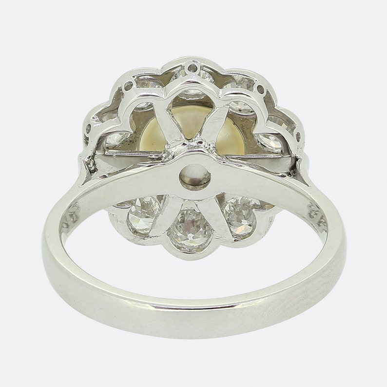 May include: A silver ring with a large pearl surrounded by a halo of smaller diamonds. The ring is set in a flower-shaped design.