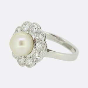 May include: A white pearl ring with a diamond halo setting. The ring is made of white metal and has a simple band.