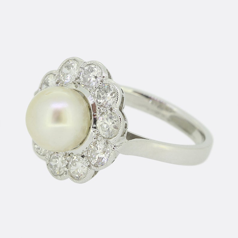May include: A white pearl ring with a diamond halo setting. The ring is made of white metal and has a simple band.