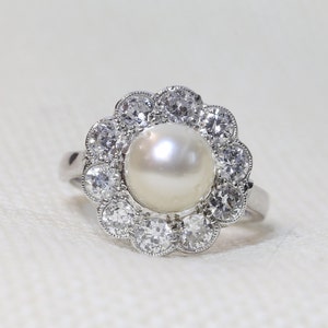 May include: A silver ring with a large white pearl surrounded by a halo of smaller diamonds.