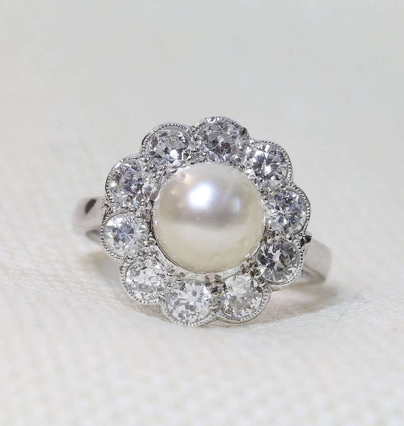 May include: A silver ring with a large white pearl surrounded by a halo of smaller diamonds.