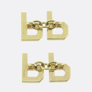 May include: Two pairs of gold cufflinks, each pair is connected by a chain. The cufflinks are shaped like the letter 'D' and have the word 'Cartier' engraved on the side.