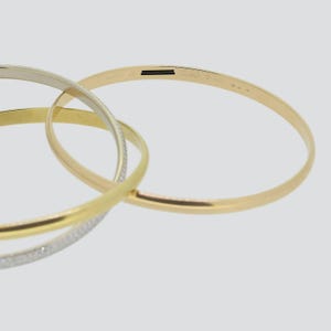 May include: Three gold bangle bracelets, one with a diamond pave design, stacked on top of each other. The bracelet on top has the inscription 'Cartier' and 'MD'.
