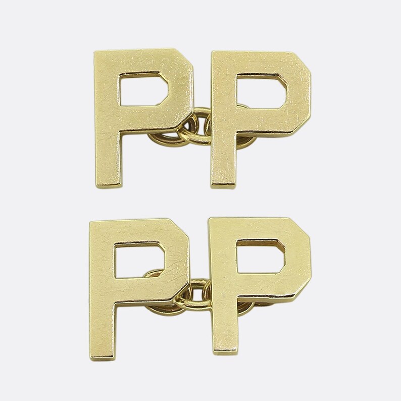 May include: Two pairs of gold letter P cufflinks. Each cufflink is a single letter P with a small chain connecting the two letters.