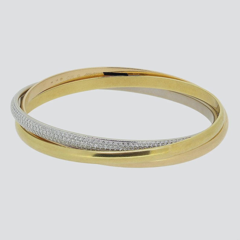 May include: A gold, silver, and rose gold bangle bracelet with a pave diamond band. The bracelet is made of three intertwined bands.