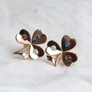 May include: A pair of gold clover-shaped earrings with red, blue, and white gemstones.