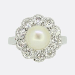 May include: A silver ring with a large white pearl surrounded by a halo of smaller diamonds.
