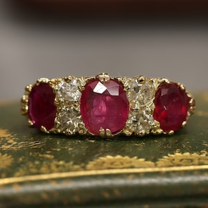 Puede incluir: Un anillo de oro con tres rubíes ovalados y pequeños diamantes.