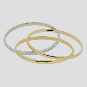 May include: Three gold bangle bracelets with a diamond-like pattern. The bracelets are stacked on top of each other. The top bracelet is white gold, the middle bracelet is rose gold, and the bottom bracelet is yellow gold.