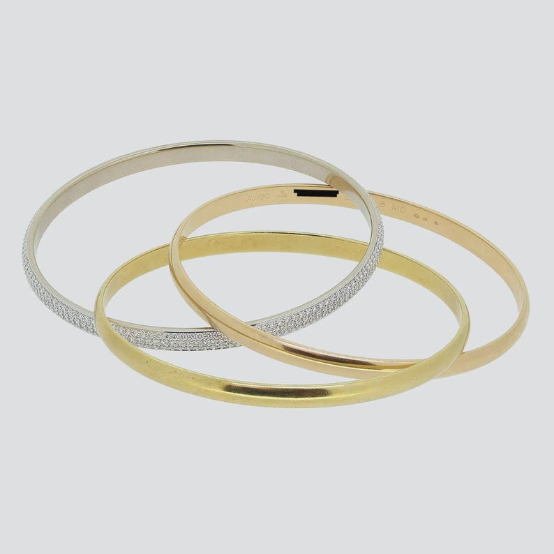 May include: Three gold bangle bracelets with a diamond-like pattern. The bracelets are stacked on top of each other. The top bracelet is white gold, the middle bracelet is rose gold, and the bottom bracelet is yellow gold.