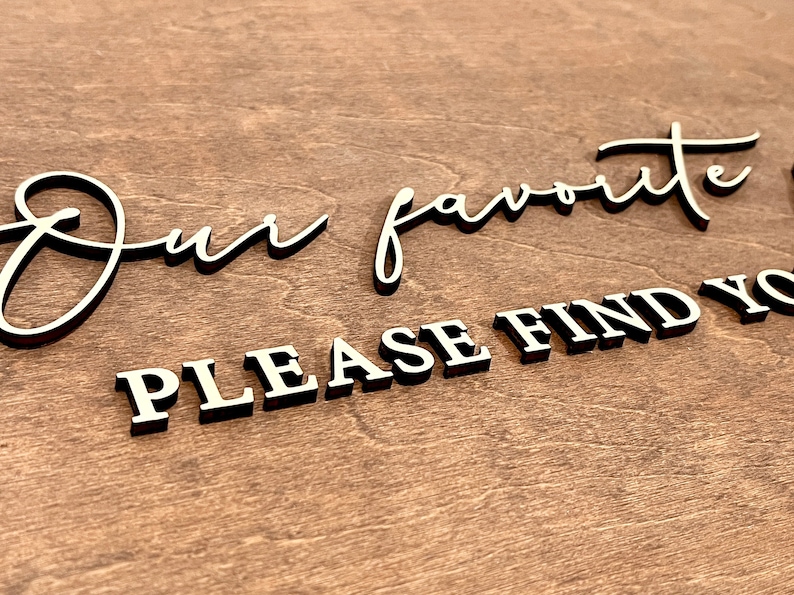 May include: A wooden sign with the text "Our favorite... Please find your..." in white lettering on a brown background.