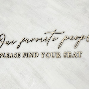 May include: A wooden sign with the text "Our favorite people" in cursive script and "Please find your seat" in block letters.